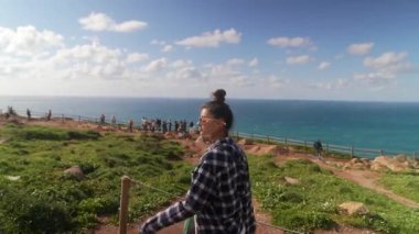 Genç bir kadın, arkadaşları sevinçle arka plandayken çarpıcı bir kıyı manzarasının tadını çıkartıyor.