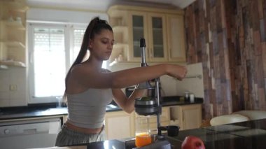 Bir kadın, modern mutfağında canlı meyveler kullanarak bir dizi taze meyve suyu üretmek için büyük bir hevesle meyve sıkacağı kullanır.