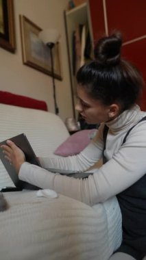 İşine çok dalmış bir kadın ev ortamında rahat bir şekilde dolaşırken dizüstü bilgisayarına odaklanmış.