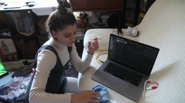 Odaklanmış genç bir kadın, rahat bir ortamda çalışırken bilgisayarını temizler ve görevleriyle meşgul olur..