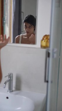 Genç bir kadın zevkli cilt bakımı rutininden zevk alır. Mutlulukla çeşitli ürünleri aynanın karşısına geçirir.