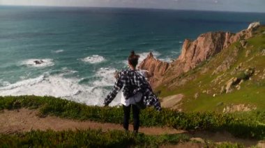 Yalnız bir insan uçurumun kenarında duruyor, çarpan okyanus dalgalarının nefes kesici güzelliğini kucaklıyor.