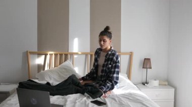 Huzurlu bir sabah sahnesinde bir insan rahat bir şekilde yatağında dizüstü bilgisayar ve akıllı telefonuyla dinleniyor.