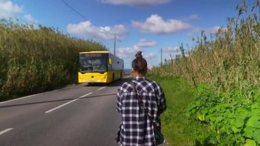 Bir insan, yemyeşil ve parlak mavi gökyüzüyle çevrili güzel bir yolda rahatça yürür.