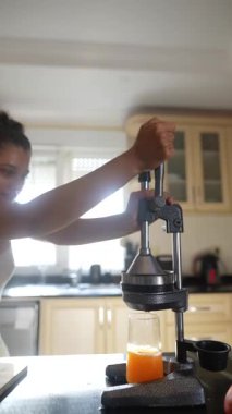 Güzel bir mutfak ortamında taze meyve suyu elde etmek için narenciye sıkma makinesini ustalıkla kullanan bir kadın.