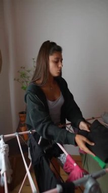 Genç bir kadın normal çamaşır işleriyle meşgul, evde kıyafetlerini dikkatlice katlıyor, sıcak ve rahat bir ortamda.
