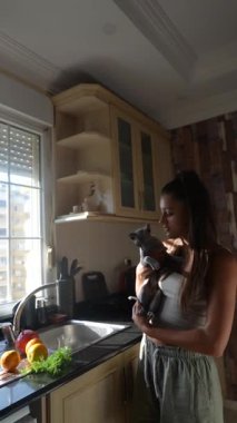 Güneşli bir mutfakta, bir kadın, taze ve renkli sebzelerle çevrili sevgili evcil hayvanıyla huzurlu bir anın tadını çıkarır.