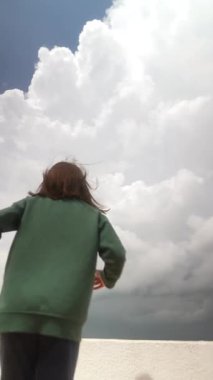 Bir çocuk dinamik ve sürekli bulutlu bir gökyüzü arkaplanı ile neşeyle etkileşime girer, saf masumiyet ve macera yakalar.