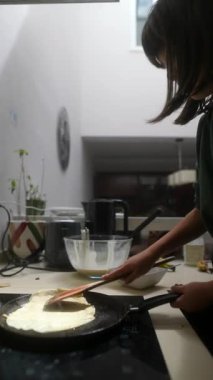 Genç bir şef, çeşitli temel yemek malzemeleriyle çevrili modern bir mutfakta ustalıkla krep hazırlar.