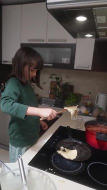 Genç bir çocuk çağdaş bir mutfakta neşeyle yemek pişiriyor, hem yaratıcılığını hem de etkileyici yeteneklerini sergiliyor.