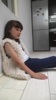 Genç bir kız düşünceli bir şekilde yumuşak yeleğiyle bir duvara yaslanıyor, gününü ve deneyimlerini derinden yansıtıyor.