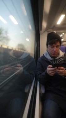 Modern iç mekanlarla çevrili bir trende otururken akıllı telefonlarına odaklanmış genç bir birey..