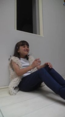 Rahat bir kıyafet giyen genç bir kız rahatça duvara yaslanıyor ve bir dizi duyguyu ifade ediyor.