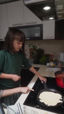 Genç bir çocuk, modern bir mutfakta leziz krepler pişiriyor. Mutfak becerilerini ve yaratıcılıklarını sergiliyor.