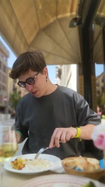 Genç bir yetişkin, güneşli bir kafede leziz bir yemeğin tadını çıkarıyor. Mutfak deneyimine kendini tamamen kaptırmış.