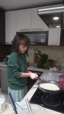 Genç bir çocuk mutlu bir şekilde krep pişirirken aynı zamanda parlak ve çağdaş bir mutfağın tadını çıkarıyor.