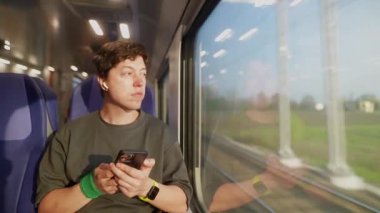 Trende seyahat ederken akıllı telefonuna odaklanan bir yolcu, modern yolculuğun özünü yakalıyor..