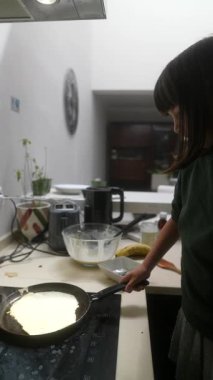 Genç bir çocuk sıcak ve davetkar bir mutfak ortamında lezzetli krepler pişirmeye odaklanır.