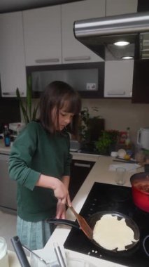 Genç bir çocuk şık bir mutfakta krep çeviriyor, eğlenceli bir yemek anı sergiliyor..