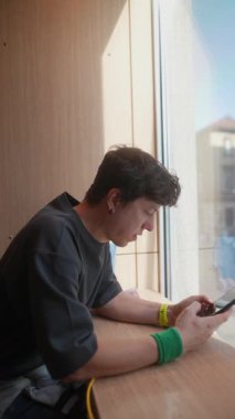 Modayı takip eden bir kafede rahat bir şekilde otururken akıllı telefonuyla derinden meşgul bir genç.