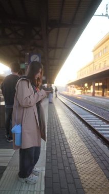 Yoğun bir tren istasyonunda bekleyen bir insan, yumuşak sabah ışığında akıllı telefonuyla kısacık anları yakalıyor.