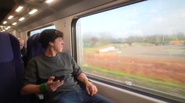 Genç bir gezgin, canlı geçen manzaraya dalmış bir şekilde, trenin penceresinden dışarı derin derin bakar.