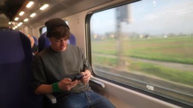 Gezici bir cihaza kendini kaptırmış genç bir insan güzel manzaralarda tren yolculuğunun tadını çıkarıyor..