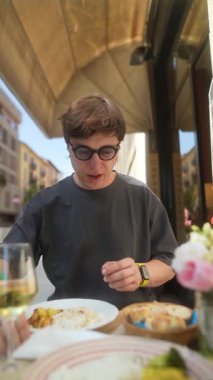 Güzel manzarayla çevrili, hareketli bir kafede yemeğin tadını çıkaran genç bir insan.