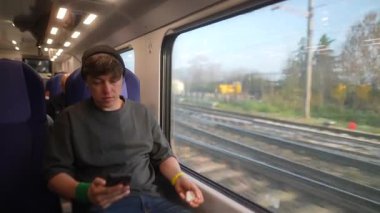 Genç bir gezgin, tren yolculuğunun keyfini çıkarırken akıllı telefon kullanır..