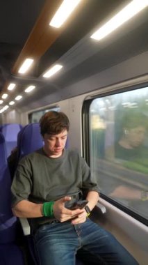 Genç bir birey, modern bir trende rahat bir şekilde seyahat ederken akıllı telefonuyla aktif olarak meşgul olur.