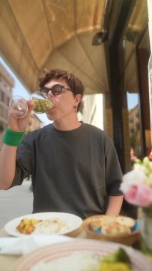 Etrafı arkadaşlarla çevrili, hareketli bir kafede gurme yemeğinin tadını çıkarırken zarif bir şekilde güzel bir şarap yudumlayan bir insan.