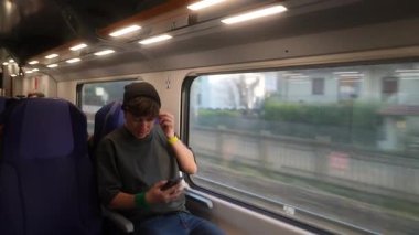 Trenle gidip gelirken akıllı telefonuyla meşgul olan genç bir adam modern seyahat deneyimlerini yakalıyor..