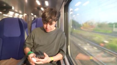 Trende seyahat ederken akıllı bir telefonla meşgul olan genç bir insan, dışarıdaki manzaranın tadını çıkarıyor..