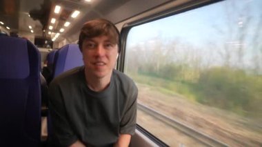 Genç bir yolcu, tren penceresinden çarpıcı manzaraya bakarken dikkatle akıllı telefon kullanıyor.