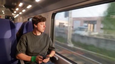 Genç bir gezgin, pencerenin dışındaki güzel ve değişen manzaradan tamamen büyülenmiş bir şekilde bir trende oturuyor.