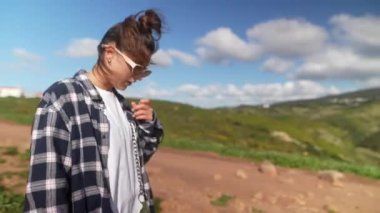 Yeşil tepeler ve çarpıcı okyanus manzaralarıyla çevrili güzel bir sahil yolunda yürüyen bir kadın yolculuğunun tadını çıkarıyor.