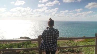 Tarz sahibi genç bir kadın, okyanusun nefes kesici kıyı manzarasında neşe içinde güzel anları yakalıyor.