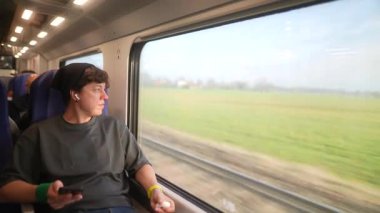 Genç bir adam trenin penceresinden dışarı bakıyor, güzel manzaraya dalmış, modern bir seyahat sergiliyor.