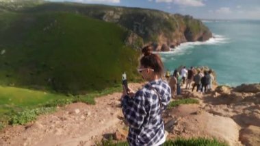 Neşeli bir kadın, resimli bir manzarada akıllı telefonunu kullanırken çarpıcı sahil manzarasından zevk alır.