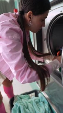 Genç bir kadın çamaşır makinesine çamaşır yüklerken şık ve modern bir çamaşırhane ortamında