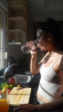 Mutlu bir insan neşeyle taze meyve suyu yapıyor. Canlı meyveler ve canlı yeşilliklerle dolu güneşli bir mutfakta.