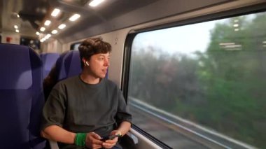 Trende rahatça dinlenen genç bir insan, pencereden dışarı bakıp güzel manzarayı seyrediyor.