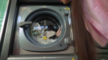 Bir kişi çamaşırların modern bir çamaşır makinesinde dönüşümünü izler, tüm çamaşır sürecinin altını çizer.