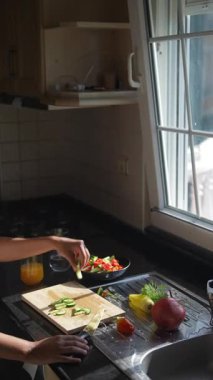 Parlak bir mutfakta, bir kadın neşe içinde renkli sebzeler hazırlarken ferahlatıcı bir içkinin tadını çıkarır.