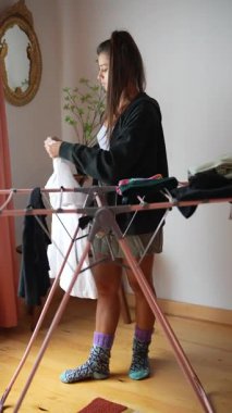 Genç bir kadın, rahat, davetkar bir odada çamaşır katlarken, günlük ev işleri sanatını sergilerken görülüyor.