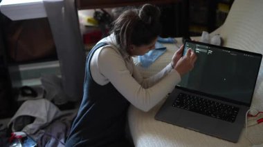 Bir öğrenci özenle bir dizüstü bilgisayarda yazıyor, karmaşık bir çalışma alanı içinde kodlama işlemiyle meşgul.