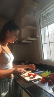 Güneşli bir mutfakta, bir kadın sağlıklı yemek hazırlamak için ideal taze domatesleri dikkatlice dilimliyor.