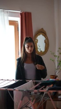 Hoş, güneşli bir odada, genç bir kadın çamaşırları dikkatlice pencerenin kenarına katlıyor, sıcak atmosferin tadını çıkarıyor.