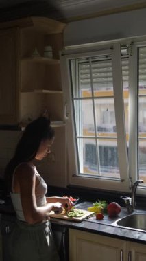 Bir kadın, sıcak güneş ışığıyla dolu parlak bir mutfakta ustalıkla taze, canlı sebzeleri doğruyor.