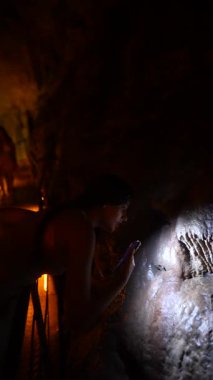 Meraklı bir kadın el fenerini kullanarak loş bir mağaradaki büyüleyici antik mağara sanatını araştırıyor.